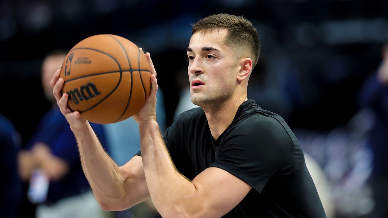 Dallas Mavericks guard John Poulakidas, in a black T-shirt, holds a basketball in shooting position during warmups.