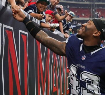 Dallas Cowboys safety Juanyeh Thomas reaches up to shake hands with young fans along the stands after a game.