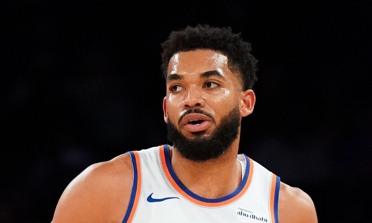 New York Knicks center Karl-Anthony Towns glances to the side in a white jersey with orange and blue trim.