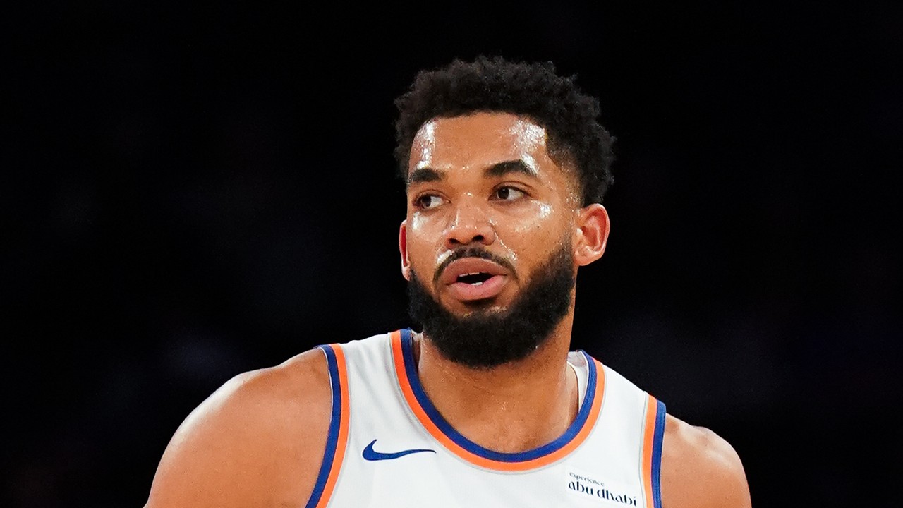 New York Knicks center Karl-Anthony Towns glances to the side in a white jersey with orange and blue trim.