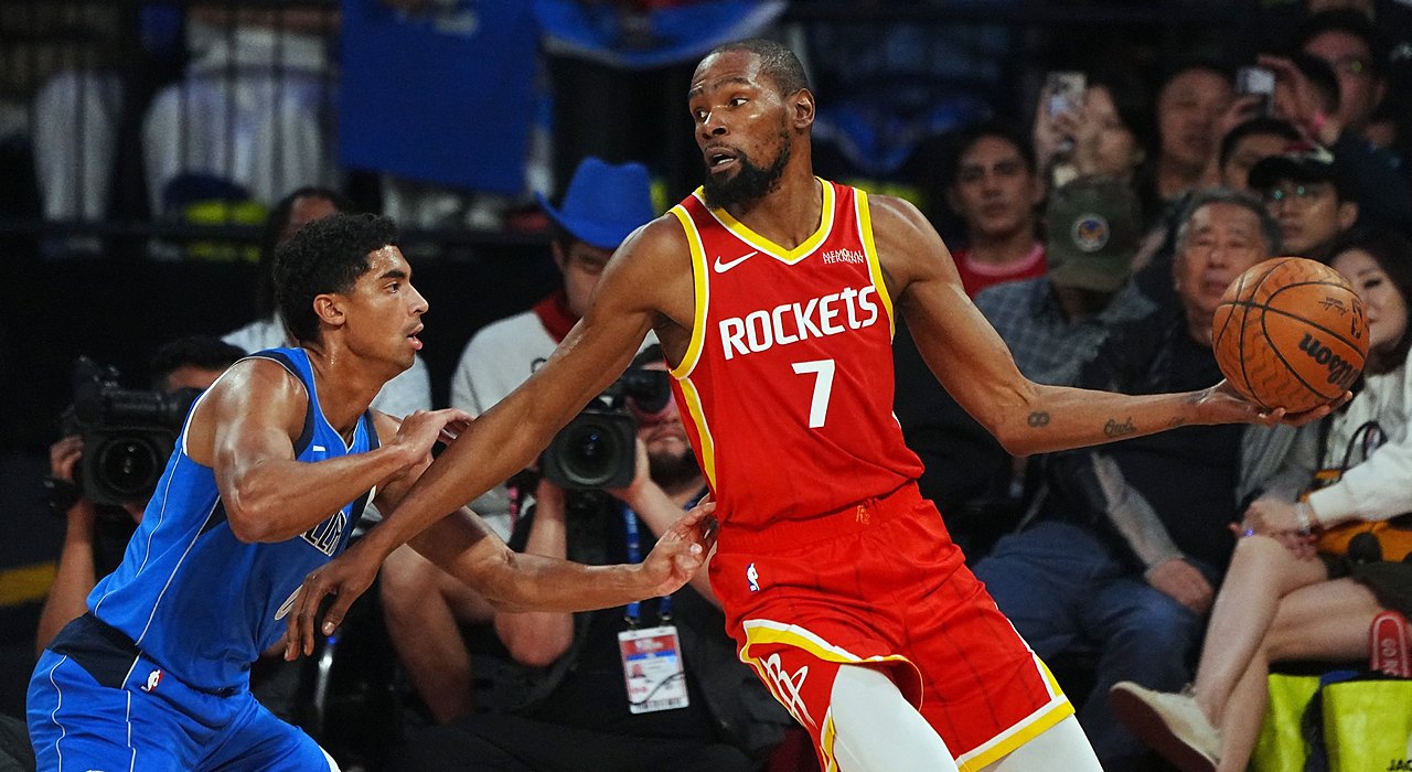 Rockets forward Kevin Durant holds the ball out wide as Mavericks guard Max Christie reaches in to defend.