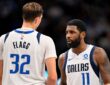 Dallas Mavericks guard Kyrie Irving talks with forward Cooper Flagg, who has his back to the camera, during a break in play.