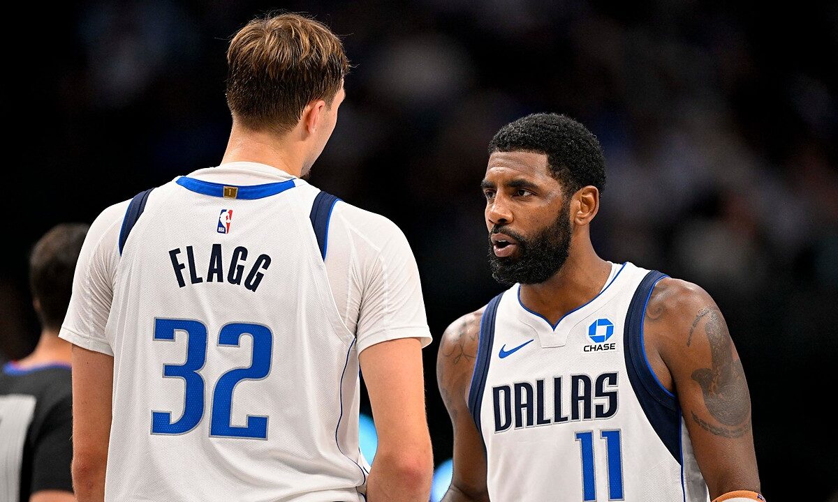 Dallas Mavericks guard Kyrie Irving talks with forward Cooper Flagg, who has his back to the camera, during a break in play.