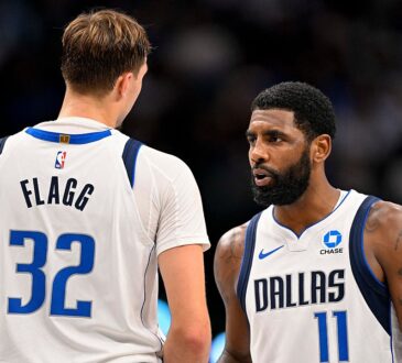 Dallas Mavericks guard Kyrie Irving talks with forward Cooper Flagg, who has his back to the camera, during a break in play.