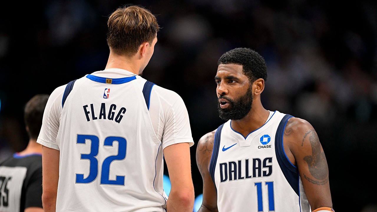 Dallas Mavericks guard Kyrie Irving talks with forward Cooper Flagg, who has his back to the camera, during a break in play.