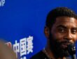 Mavericks guard Kyrie Irving smiles while speaking into a microphone in front of an NBA China Games backdrop.