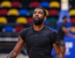 Dallas Mavericks guard Kyrie Irving looks up during practice, with rows of multicolored arena seats behind him.