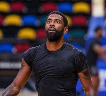 Dallas Mavericks guard Kyrie Irving looks up during practice, with rows of multicolored arena seats behind him.