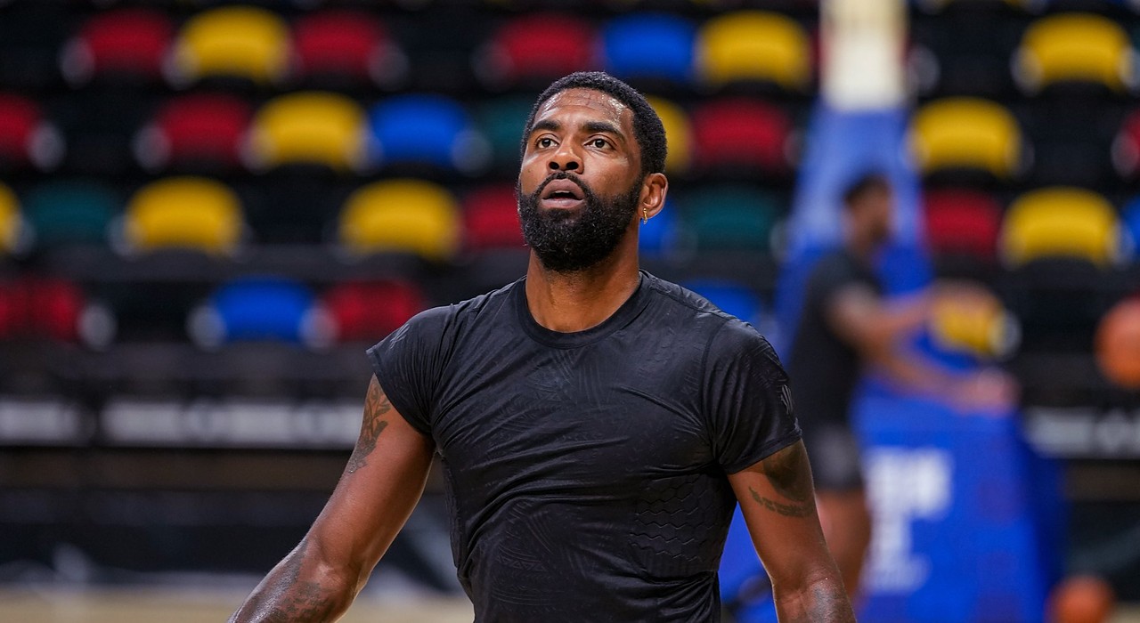 Dallas Mavericks guard Kyrie Irving looks up during practice, with rows of multicolored arena seats behind him.