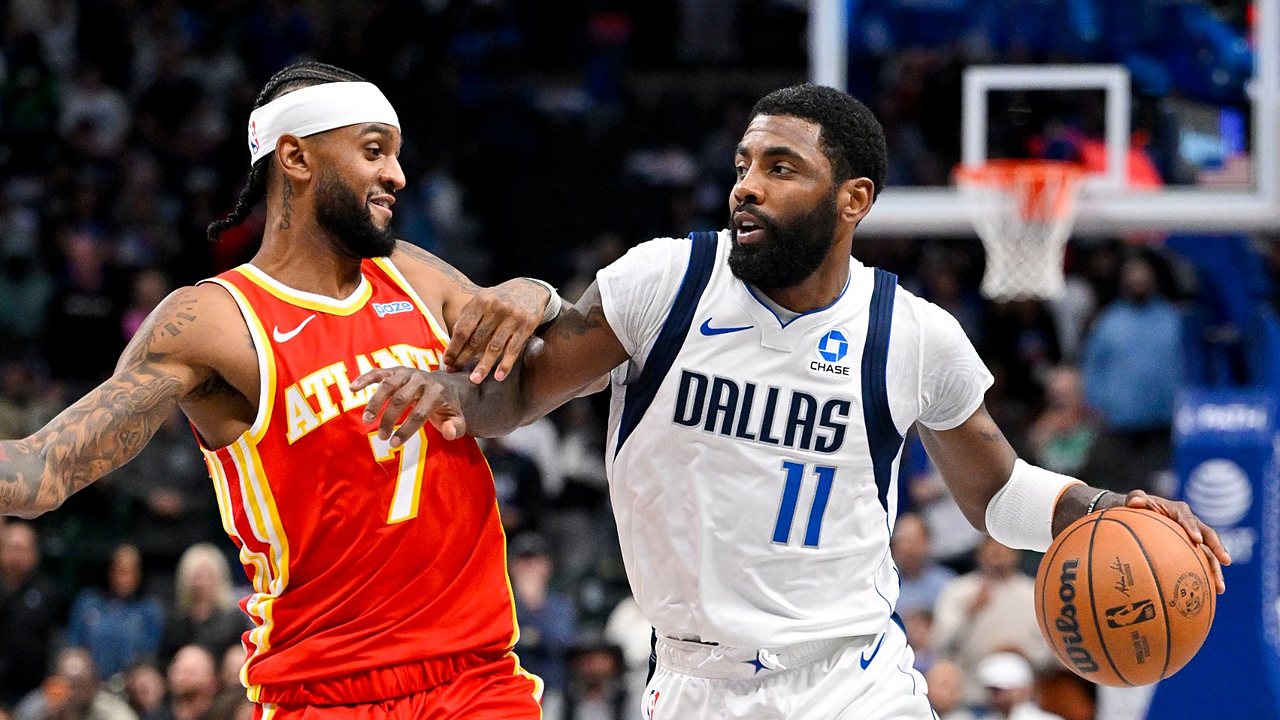 Dallas Mavericks guard Kyrie Irving dribbles past Atlanta Hawks guard Nickeil Alexander-Walker, who reaches across his arm.