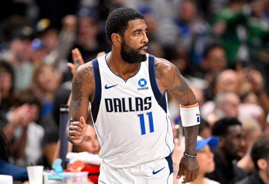 Dallas Mavericks guard Kyrie Irving glances over his shoulder while jogging down the court with his fist clenched.