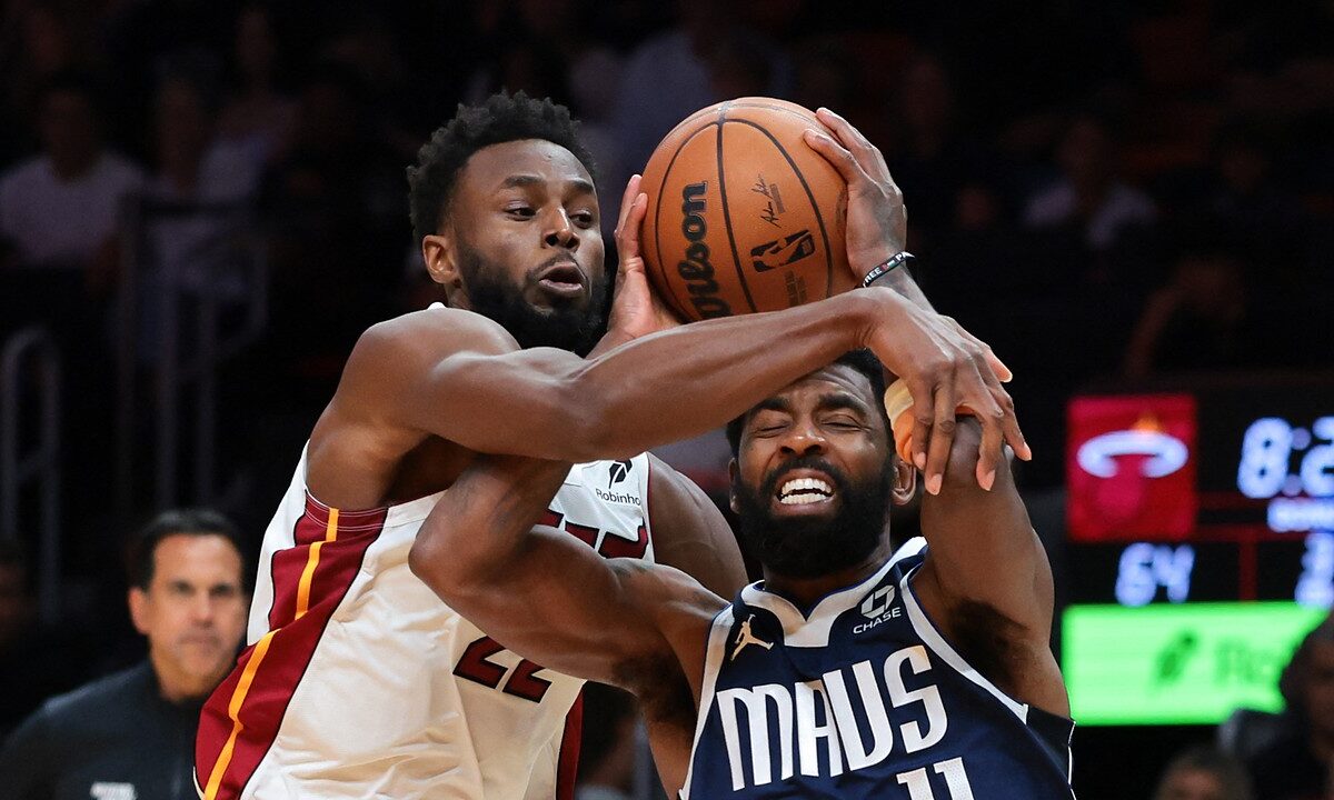 Dallas Mavericks guard Kyrie Irving grimaces as Miami Heat forward Andrew Wiggins reaches across him to grab the ball.