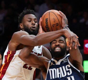 Dallas Mavericks guard Kyrie Irving grimaces as Miami Heat forward Andrew Wiggins reaches across him to grab the ball.