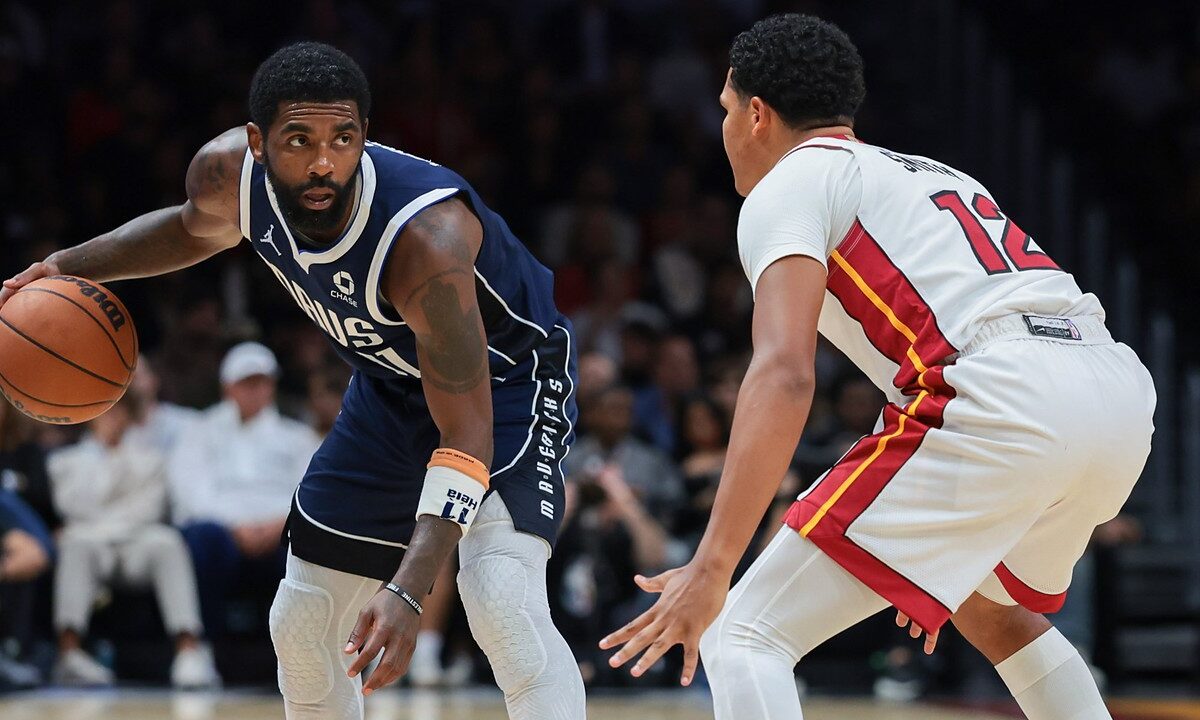 Dallas Mavericks guard Kyrie Irving dribbles with his right hand as Miami Heat guard Dru Smith crouches to defend.
