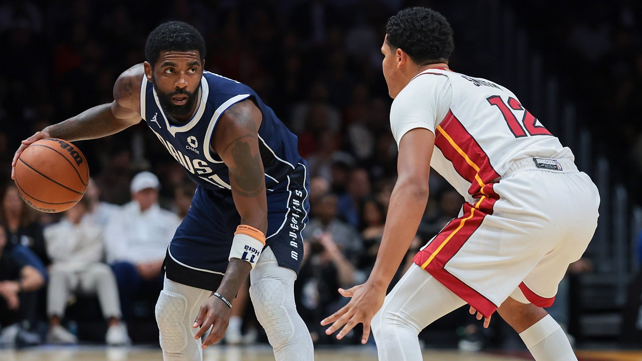 Dallas Mavericks guard Kyrie Irving dribbles with his right hand as Miami Heat guard Dru Smith crouches to defend.