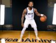 Mavericks guard Kyrie Irving poses in a low dribbling stance in his white home uniform on a studio court.