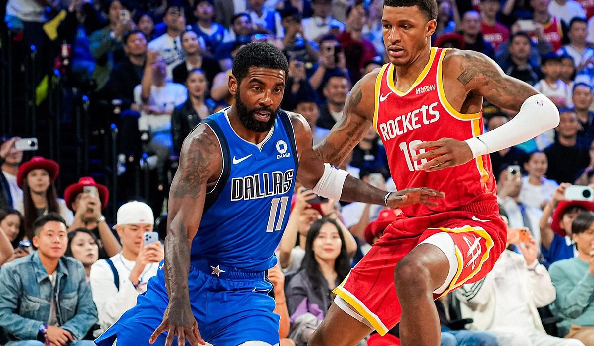 Mavericks guard Kyrie Irving dribbles low as Rockets forward Jabari Smith Jr. defends in front of a packed crowd.