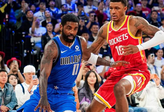 Mavericks guard Kyrie Irving dribbles low as Rockets forward Jabari Smith Jr. defends in front of a packed crowd.