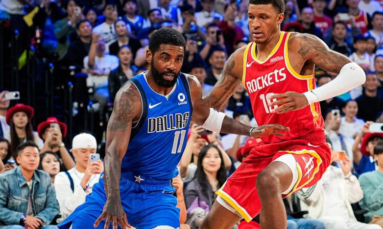 Mavericks guard Kyrie Irving dribbles low as Rockets forward Jabari Smith Jr. defends in front of a packed crowd.