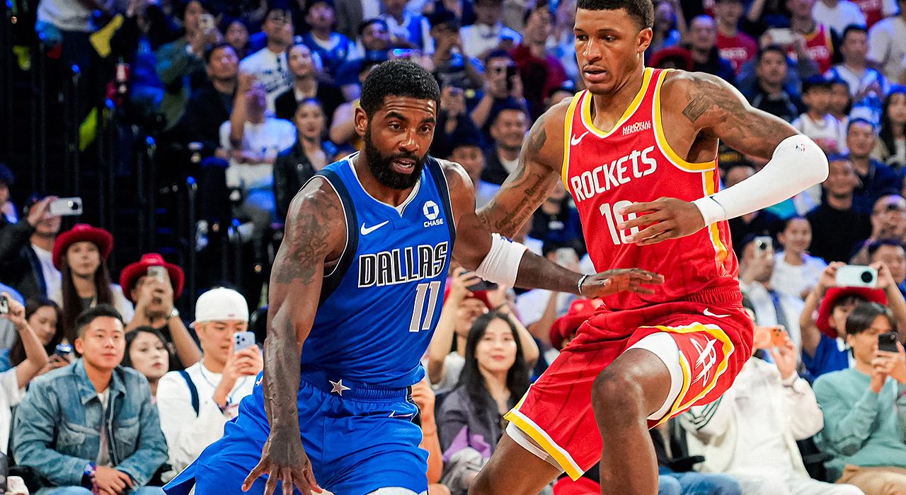Mavericks guard Kyrie Irving dribbles low as Rockets forward Jabari Smith Jr. defends in front of a packed crowd.