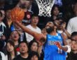 Mavericks guard Kyrie Irving extends for a reverse layup under the rim as fans behind the basket react.