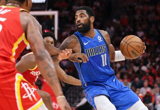 Dallas Mavericks guard Kyrie Irving dribbles past Houston Rockets defenders with the ball in his left hand.