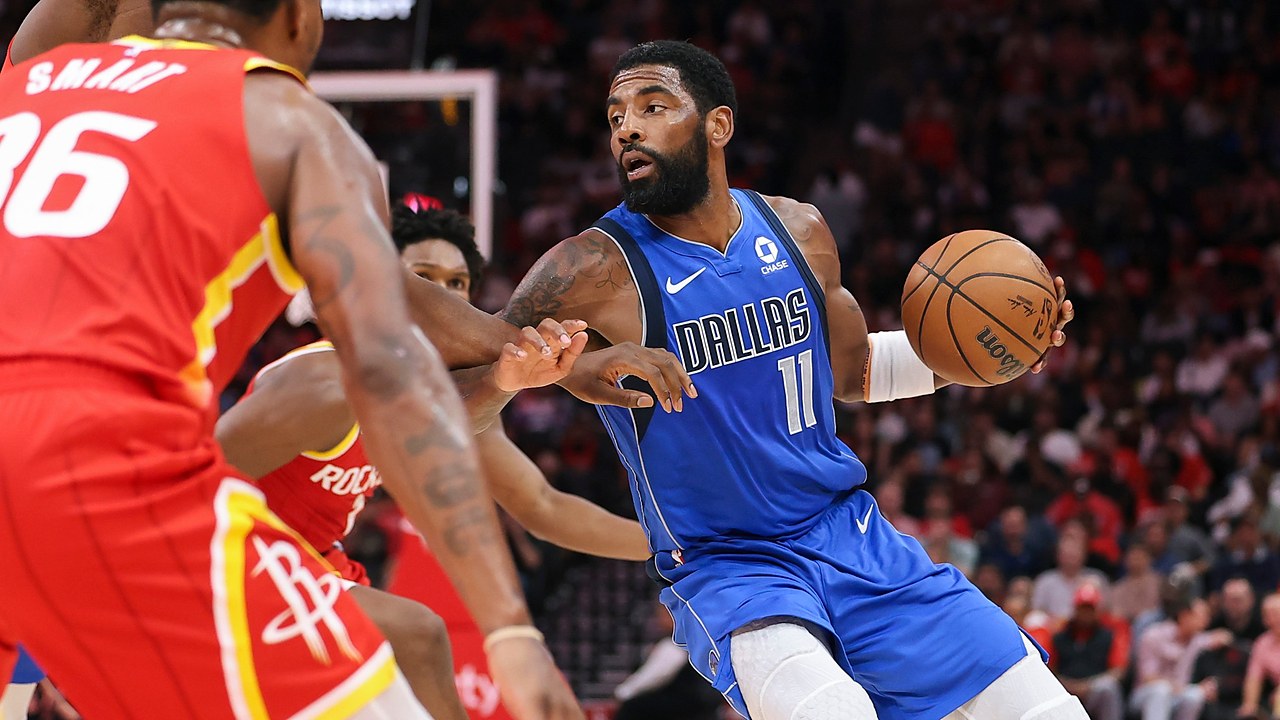 Dallas Mavericks guard Kyrie Irving dribbles past Houston Rockets defenders with the ball in his left hand.