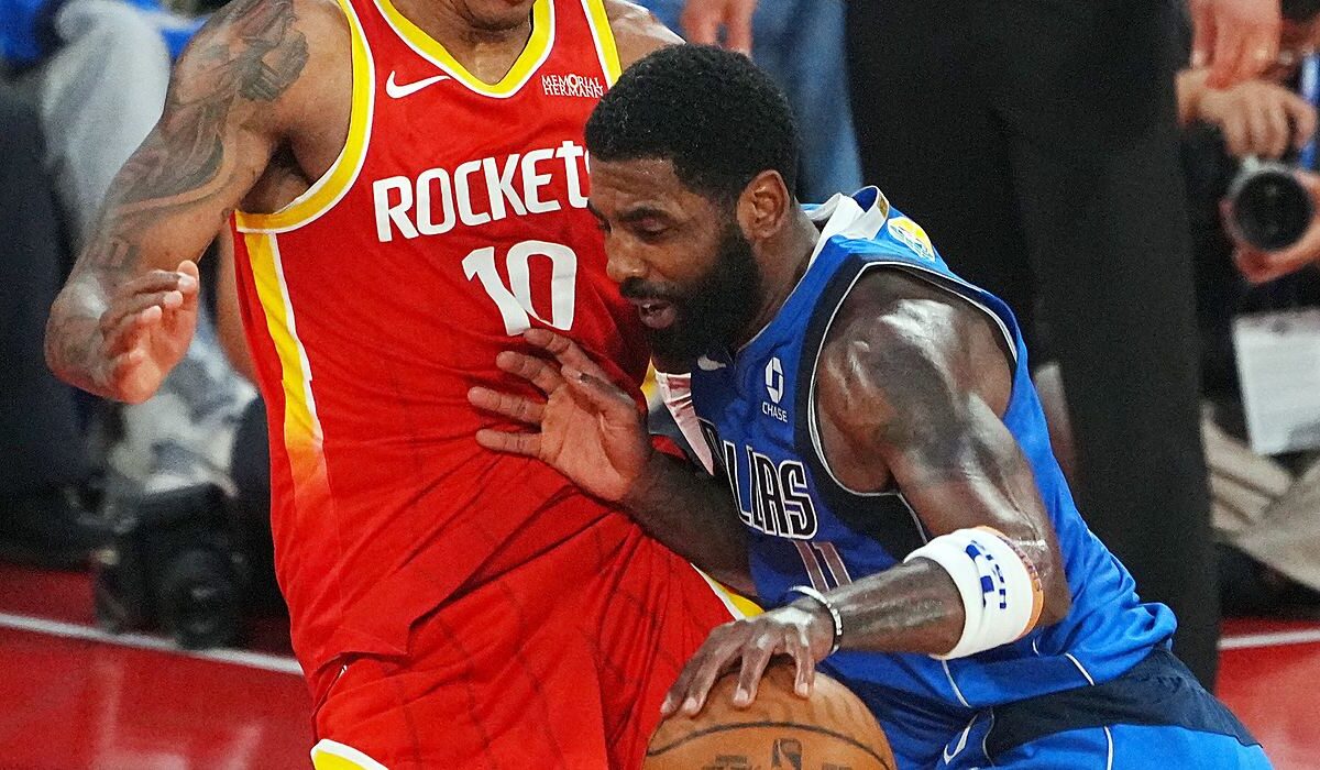 Mavericks guard Kyrie Irving lowers his shoulder and drives into Rockets forward Jabari Smith Jr. while dribbling.