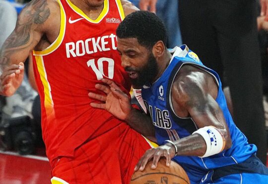 Mavericks guard Kyrie Irving lowers his shoulder and drives into Rockets forward Jabari Smith Jr. while dribbling.