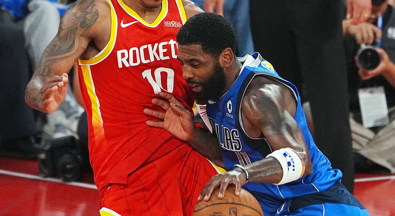 Mavericks guard Kyrie Irving lowers his shoulder and drives into Rockets forward Jabari Smith Jr. while dribbling.