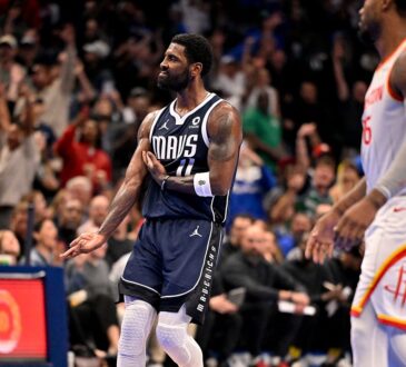 Mavericks guard Kyrie Irving gestures in celebration as fans cheer behind him.
