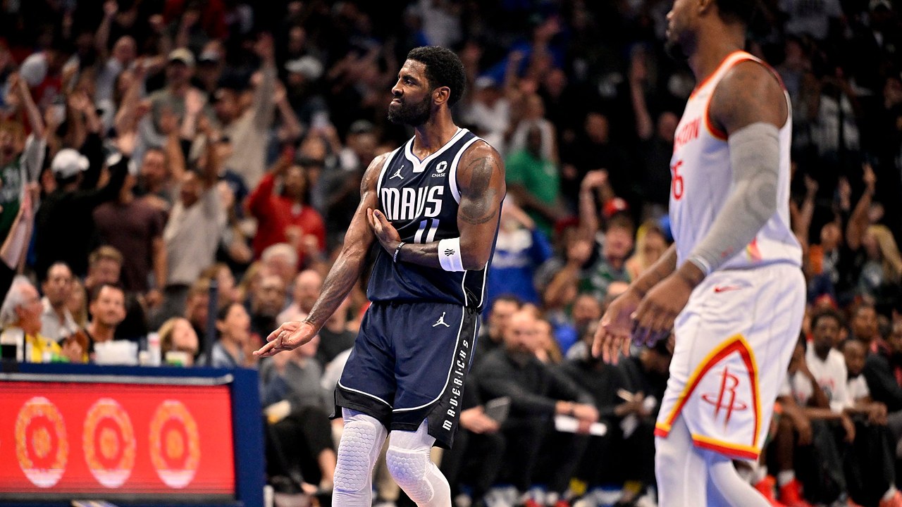 Mavericks guard Kyrie Irving gestures in celebration as fans cheer behind him.