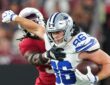 Dallas Cowboys tight end Luke Schoonmaker clutches the ball and shoves an Arizona Cardinals safety away with his free arm.