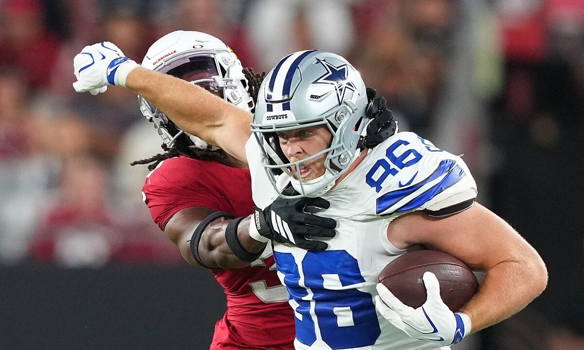 Dallas Cowboys tight end Luke Schoonmaker clutches the ball and shoves an Arizona Cardinals safety away with his free arm.
