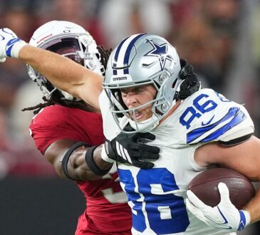 Dallas Cowboys tight end Luke Schoonmaker clutches the ball and shoves an Arizona Cardinals safety away with his free arm.