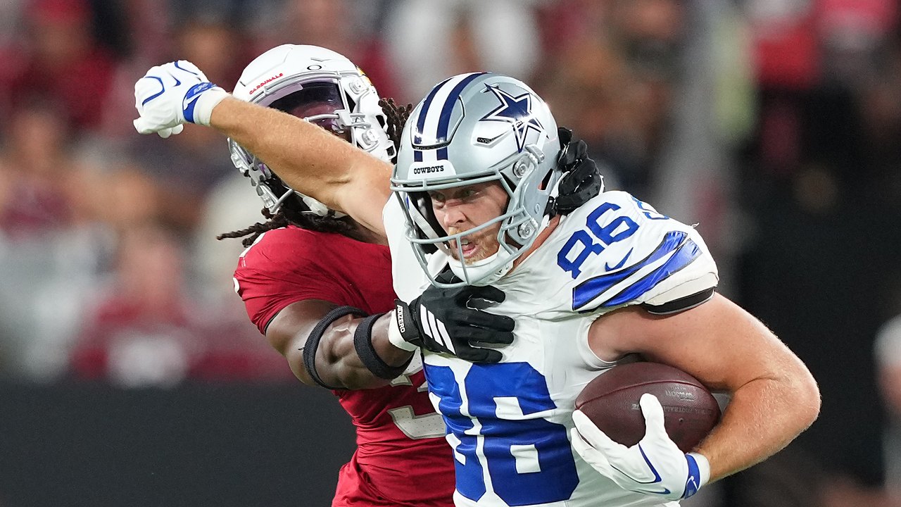 Dallas Cowboys tight end Luke Schoonmaker clutches the ball and shoves an Arizona Cardinals safety away with his free arm.