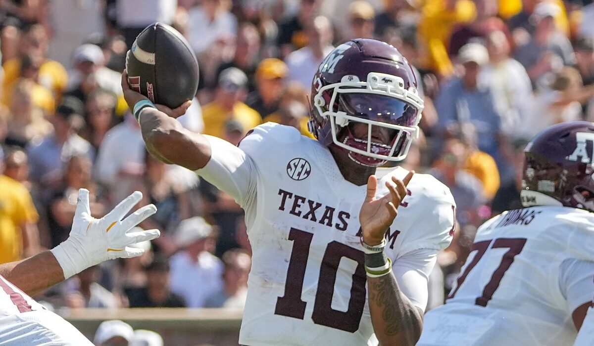 Texas A&M quarterback Marcel Reed cocks his arm back to throw as a defender's gloved hand reaches in from the left.