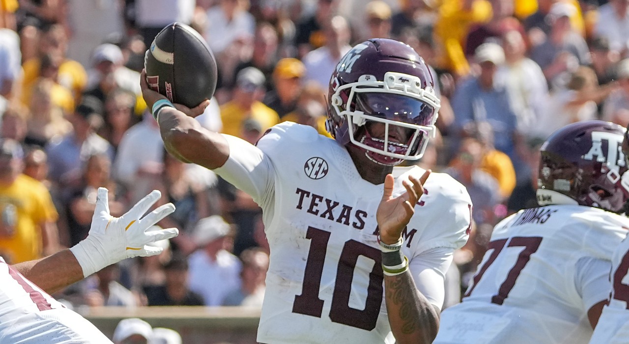 Texas A&M quarterback Marcel Reed cocks his arm back to throw as a defender's gloved hand reaches in from the left.