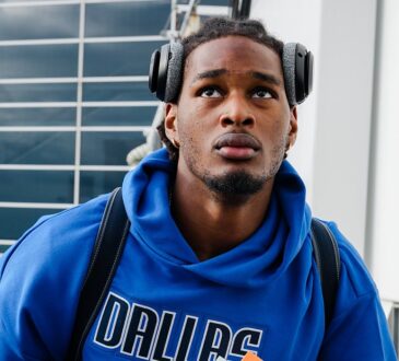 Dallas Mavericks rookie forward Morez Johnson Jr. climbs the stairs to the team plane wearing a blue Dallas hoodie and headphones.