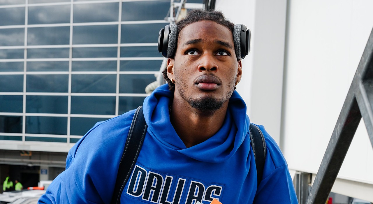 Dallas Mavericks rookie forward Morez Johnson Jr. climbs the stairs to the team plane wearing a blue Dallas hoodie and headphones.