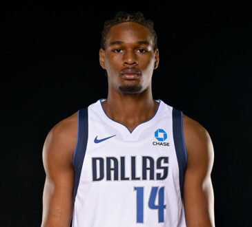 Mavericks rookie forward Morez Johnson Jr. stands facing the camera in a white Dallas No. 14 jersey against a black backdrop.