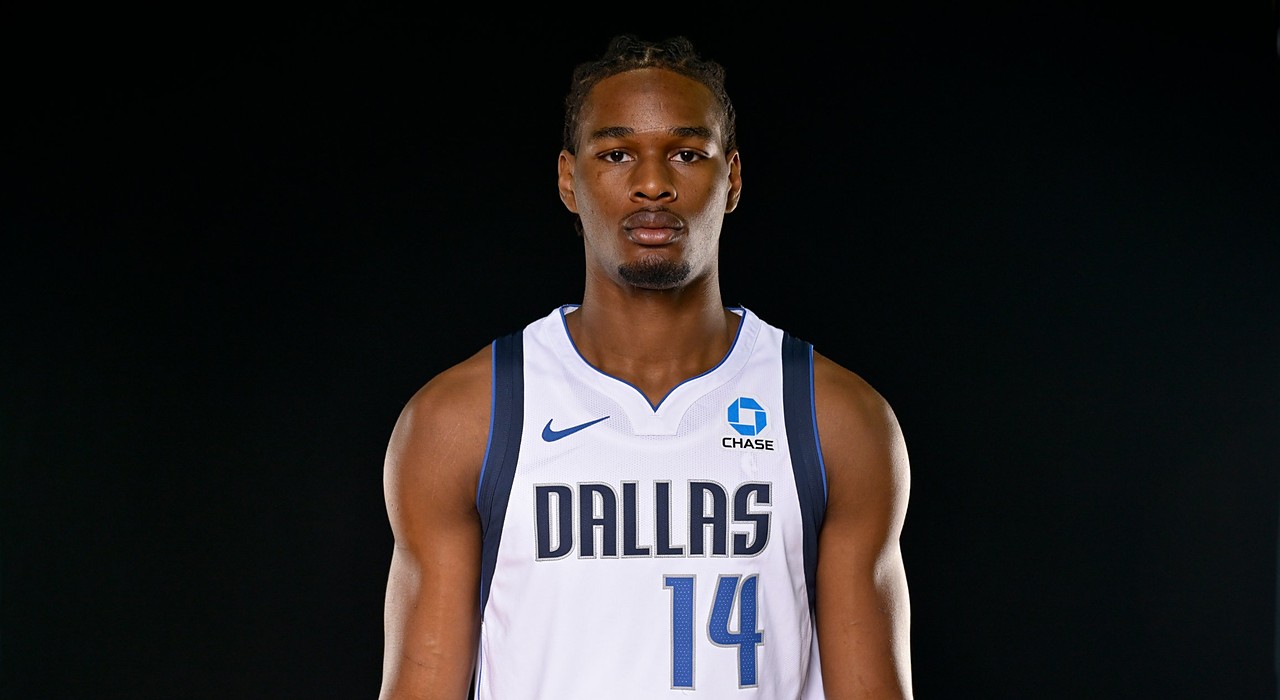 Mavericks rookie forward Morez Johnson Jr. stands facing the camera in a white Dallas No. 14 jersey against a black backdrop.