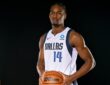 Mavericks forward Morez Johnson Jr. holds a basketball at his waist while posing in his white home jersey against a black backdrop.