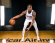 Dallas Mavericks forward Morez Johnson Jr. crouches in a dribbling stance on a hardwood court between two studio lights.