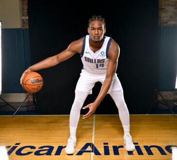Dallas Mavericks forward Morez Johnson Jr. crouches in a dribbling stance on a hardwood court between two studio lights.