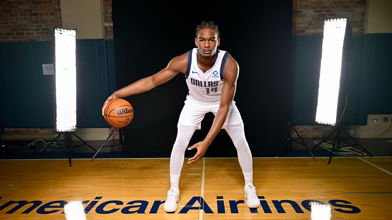 Dallas Mavericks forward Morez Johnson Jr. crouches in a dribbling stance on a hardwood court between two studio lights.