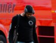 Dallas Mavericks forward Naji Marshall walks past a red bus on the tarmac, wearing headphones and carrying travel bags.
