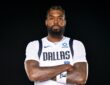 Mavericks forward Naji Marshall poses with his arms crossed in a white Dallas jersey against a black backdrop.