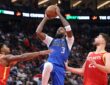 Dallas Mavericks forward Naji Marshall rises with the ball overhead between two Houston Rockets defenders.