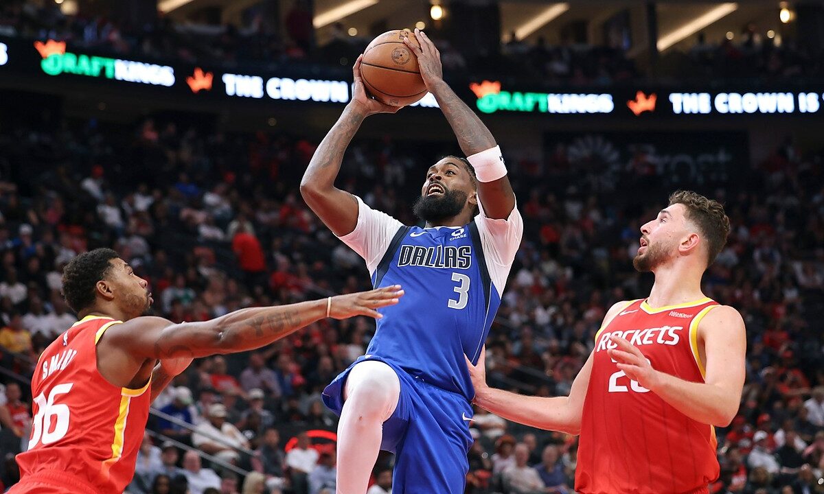 Dallas Mavericks forward Naji Marshall rises with the ball overhead between two Houston Rockets defenders.